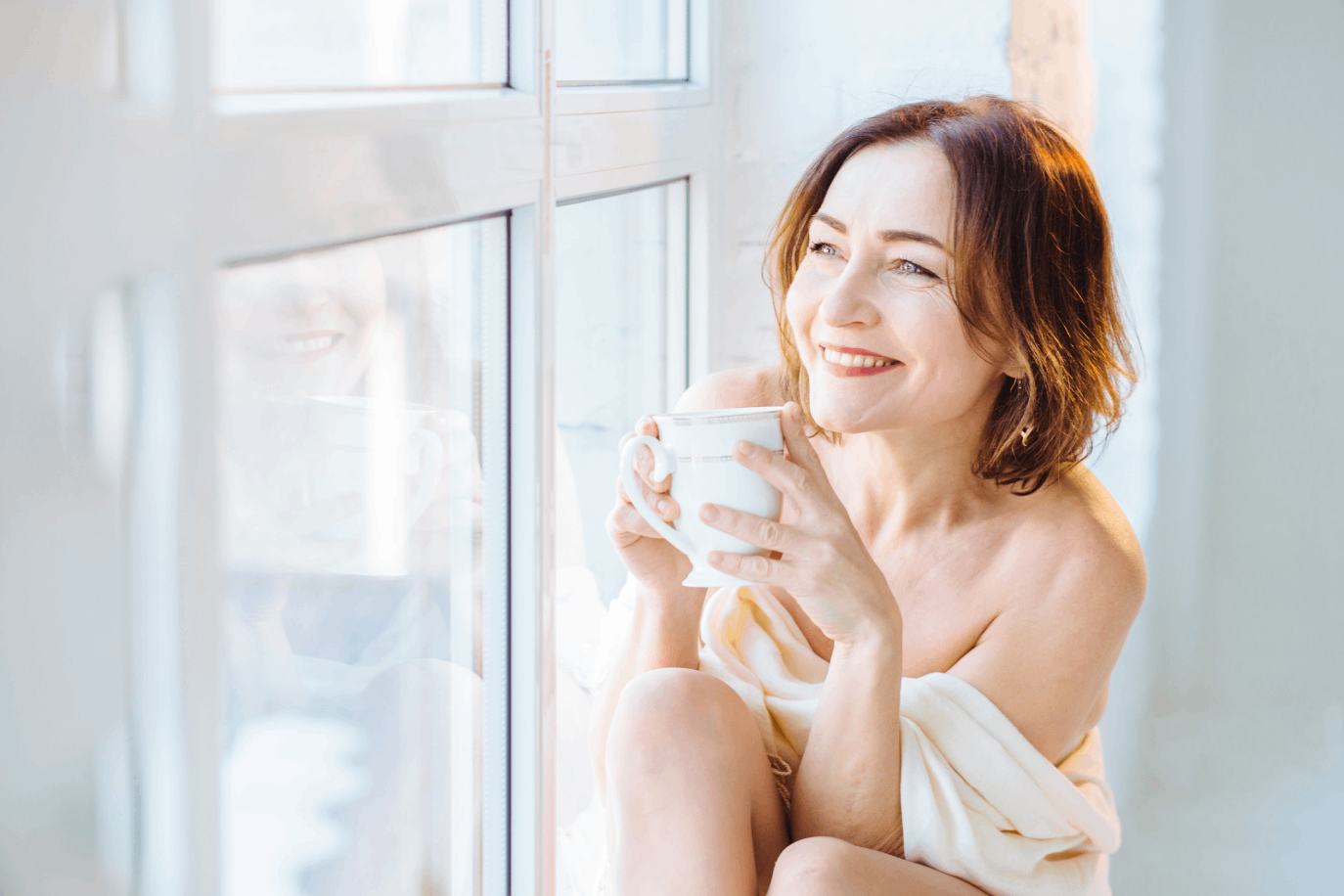 Woman sitting in a windowsill drinking coffee after microneedling session