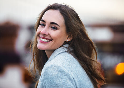 GLP-1 for weight loss results seen in a smiling woman in a grey coat outdoors.