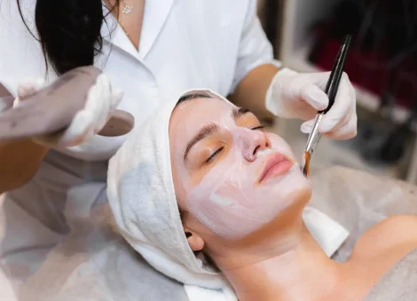Custom facial treatment in progress as an esthetician applies a creamy mask to a relaxed client's face with a brush.
