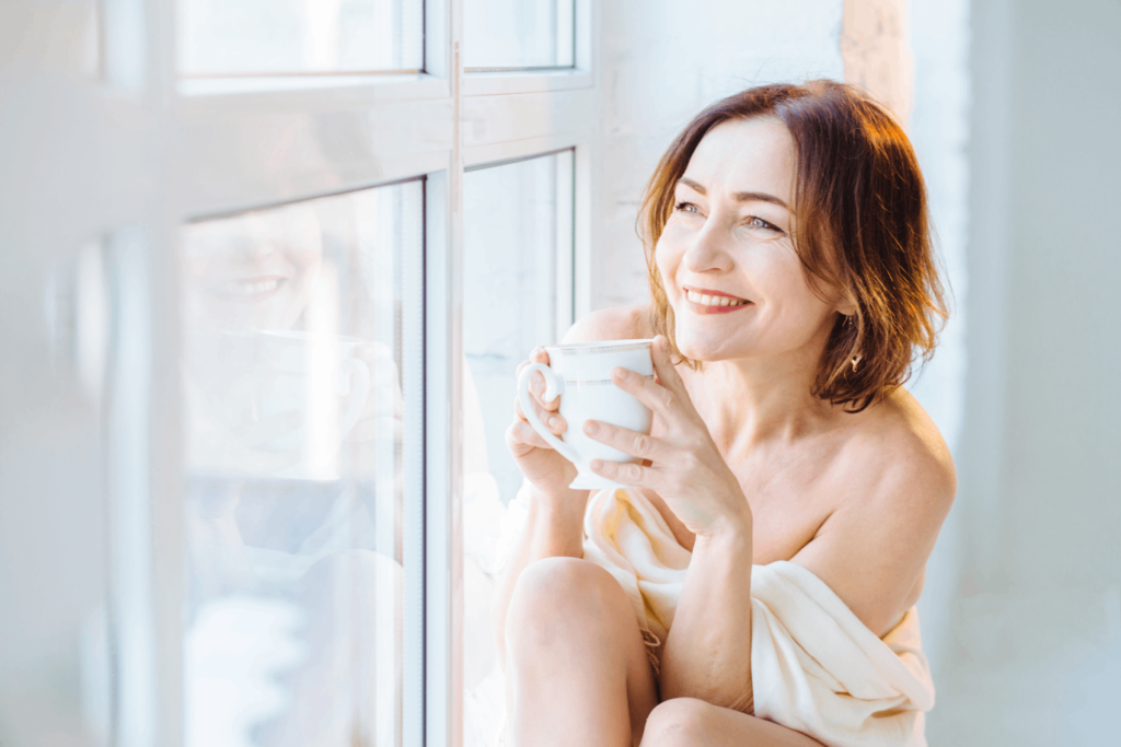Hormone pellet therapy benefits shown by a relaxed, smiling woman enjoying a warm drink by the window.