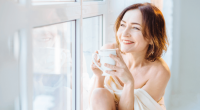 Hormone pellet therapy benefits shown by a relaxed, smiling woman enjoying a warm drink by the window.