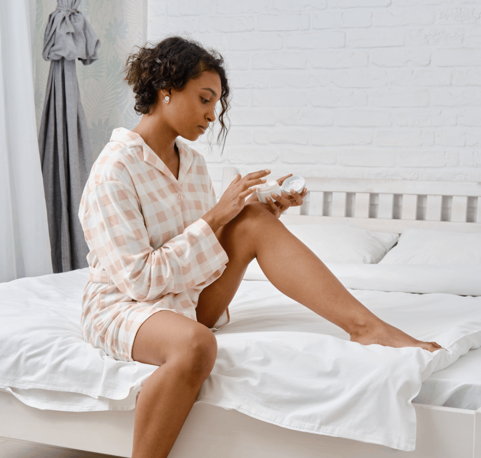 woman sitting on a bed applying lotion after having laser hair removal.