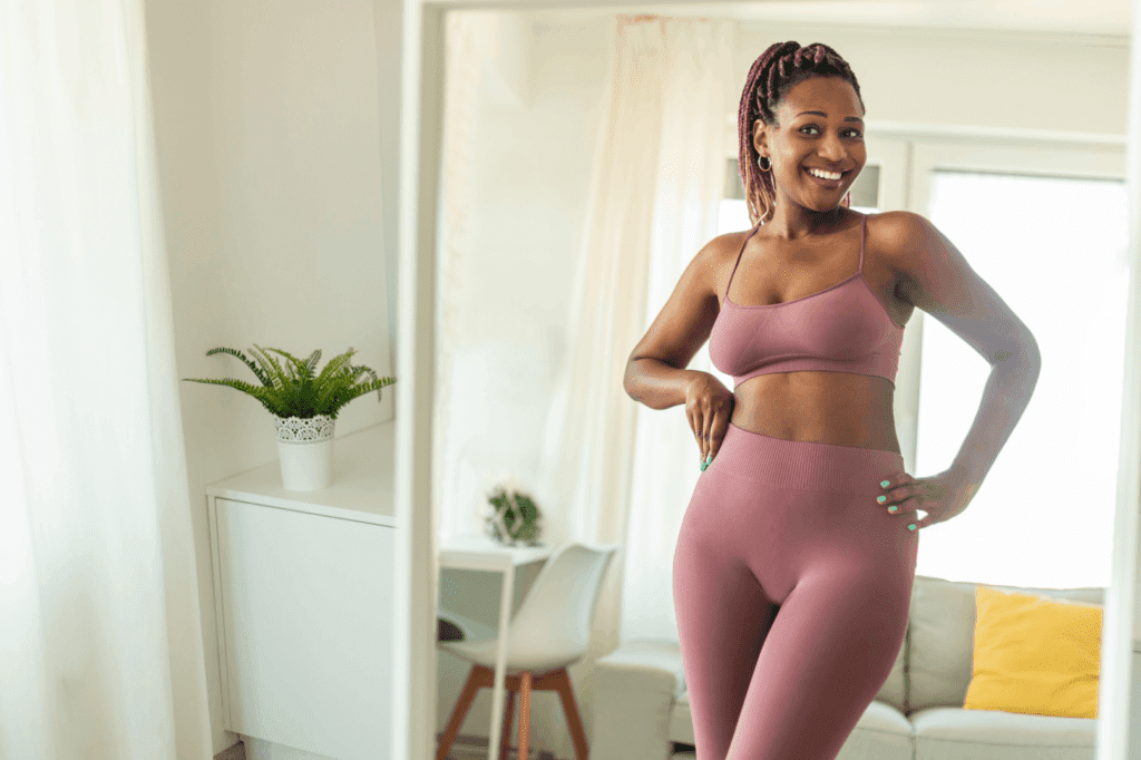 GLP-1 weight loss shown by a fit woman smiling confidently in front of a mirror wearing matching workout clothes.