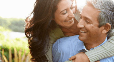 Smiling middle-aged couple embracing outdoors in sunlight, representing restored intimacy and vitality from hormone replacement therapy.