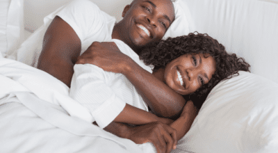 Smiling couple lying together in bed representing restored intimacy and connection from hormone replacement therapy.