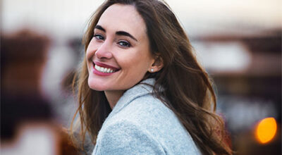 GLP-1 for weight loss results seen in a smiling woman in a grey coat outdoors.