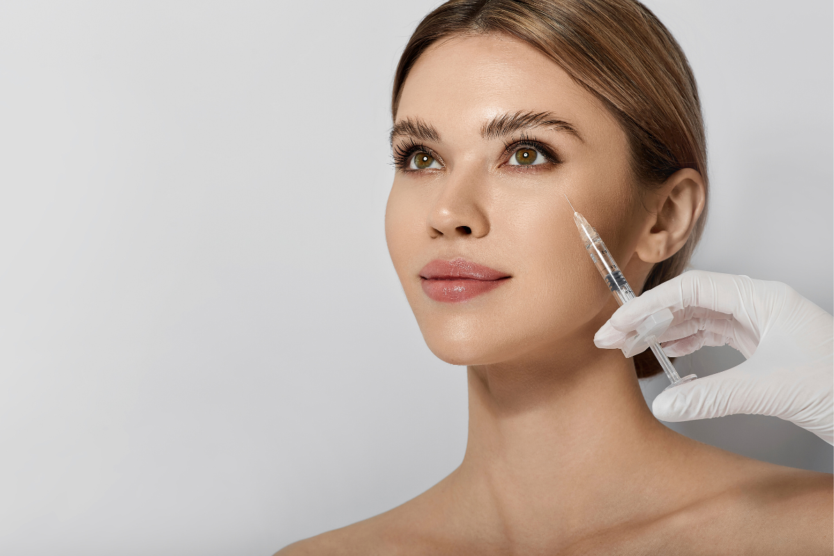 Botox for frown lines applied to a young woman’s forehead by a gloved hand holding a syringe.