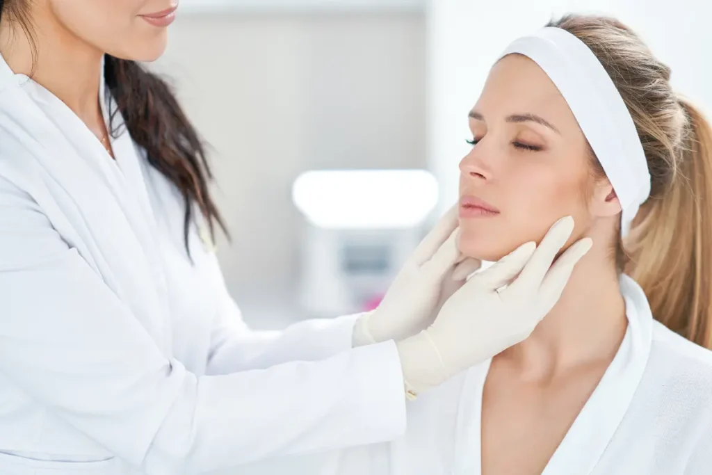 Facial assessment by a gloved esthetician examining a client's jawline and skin before an anti-aging treatment.