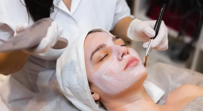 Custom facial treatment in progress as an esthetician applies a creamy mask to a relaxed client's face with a brush.